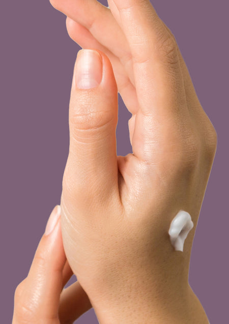 Hand with a dab of white hand cream on the back against a plum background