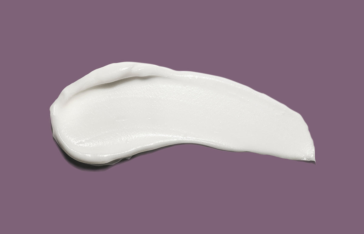 Swatch of white hand cream smeared across a plum purple background