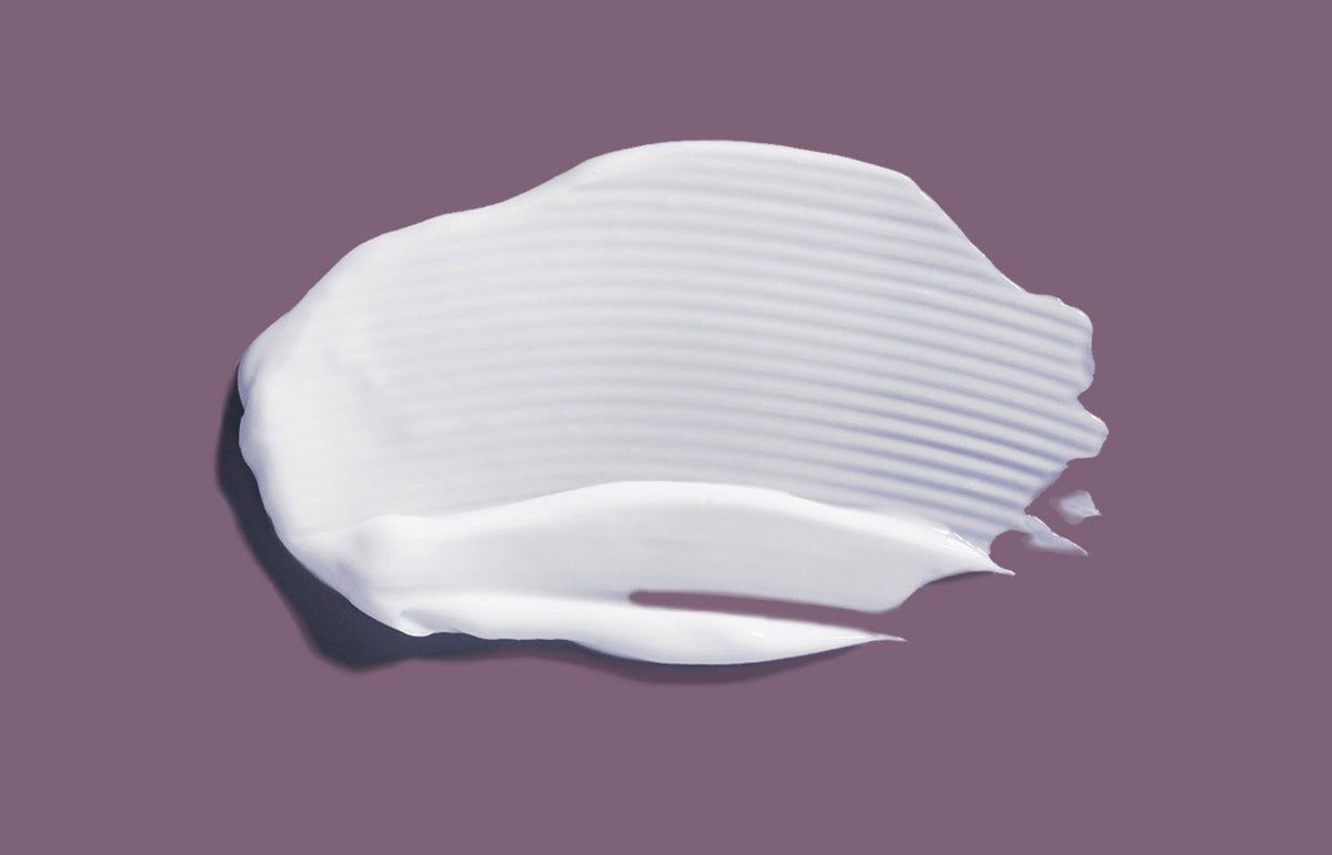 A swatch of white body lotion on a soft mauve background
