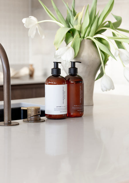 Amber Therapy bottles beside a vase of white tulips on a white kitchen benchtop