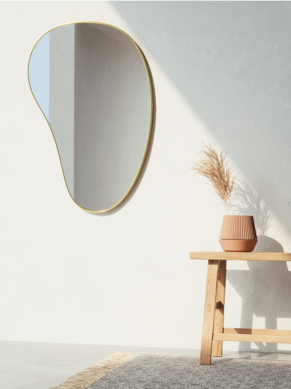 Umbra Hubba pebble mirror in brass on a pale wall above dried grasses
