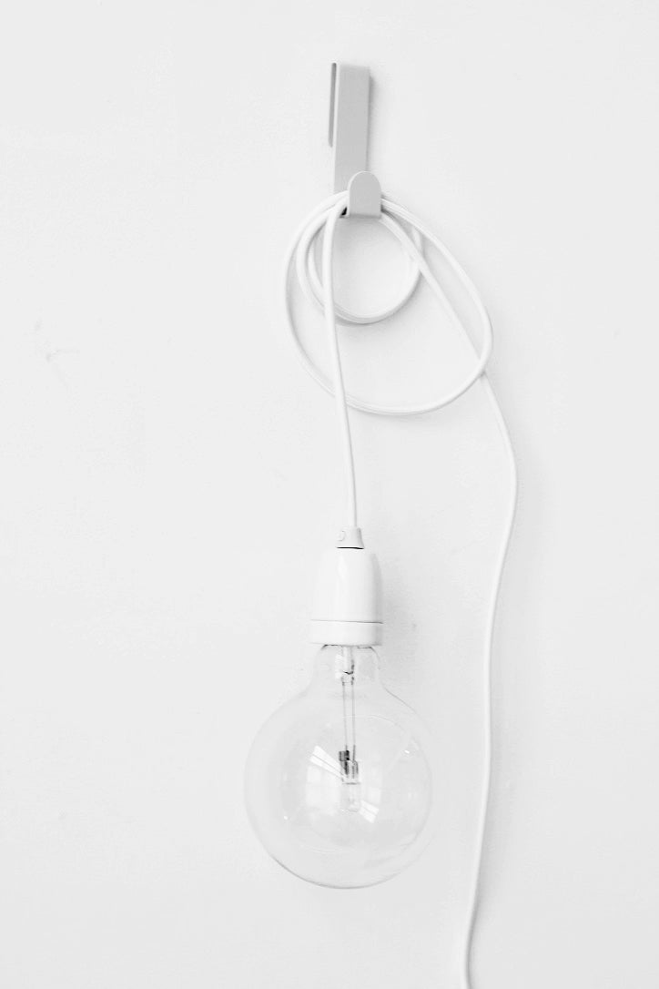 White plug-in pendant cord looped over a wall hook with a clear bulb