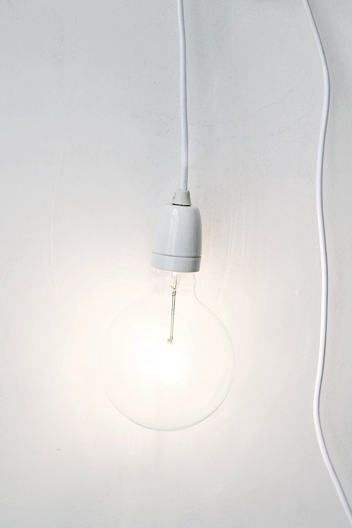 Minimalist plug-in pendant light with a large clear bulb hanging from a white cord against a white wall.