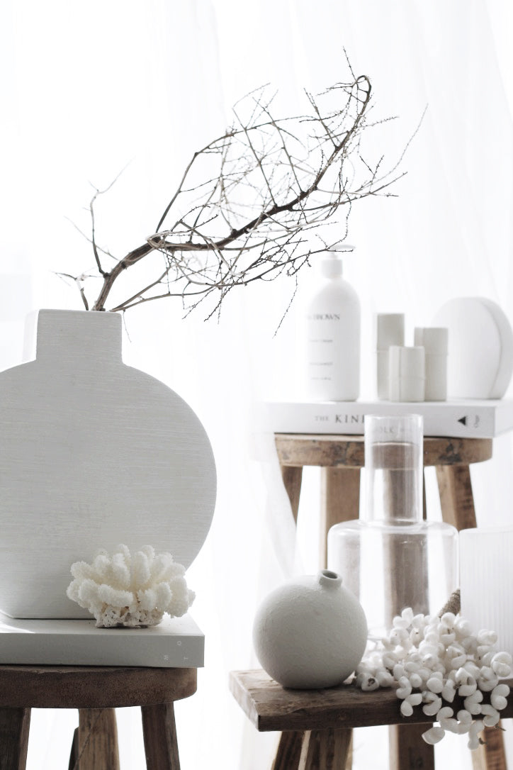 Small recycled teak benches styled with a white vase, coral and skincare