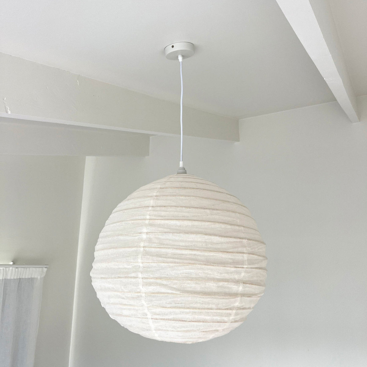 The globe shade hanging from a white ceiling beside an exposed beam