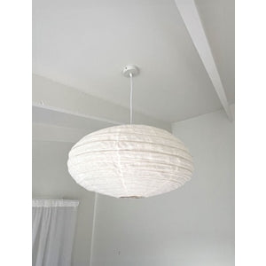 White oval linen pendant shade hanging from a ceiling rose in a pale room with a sloped beam