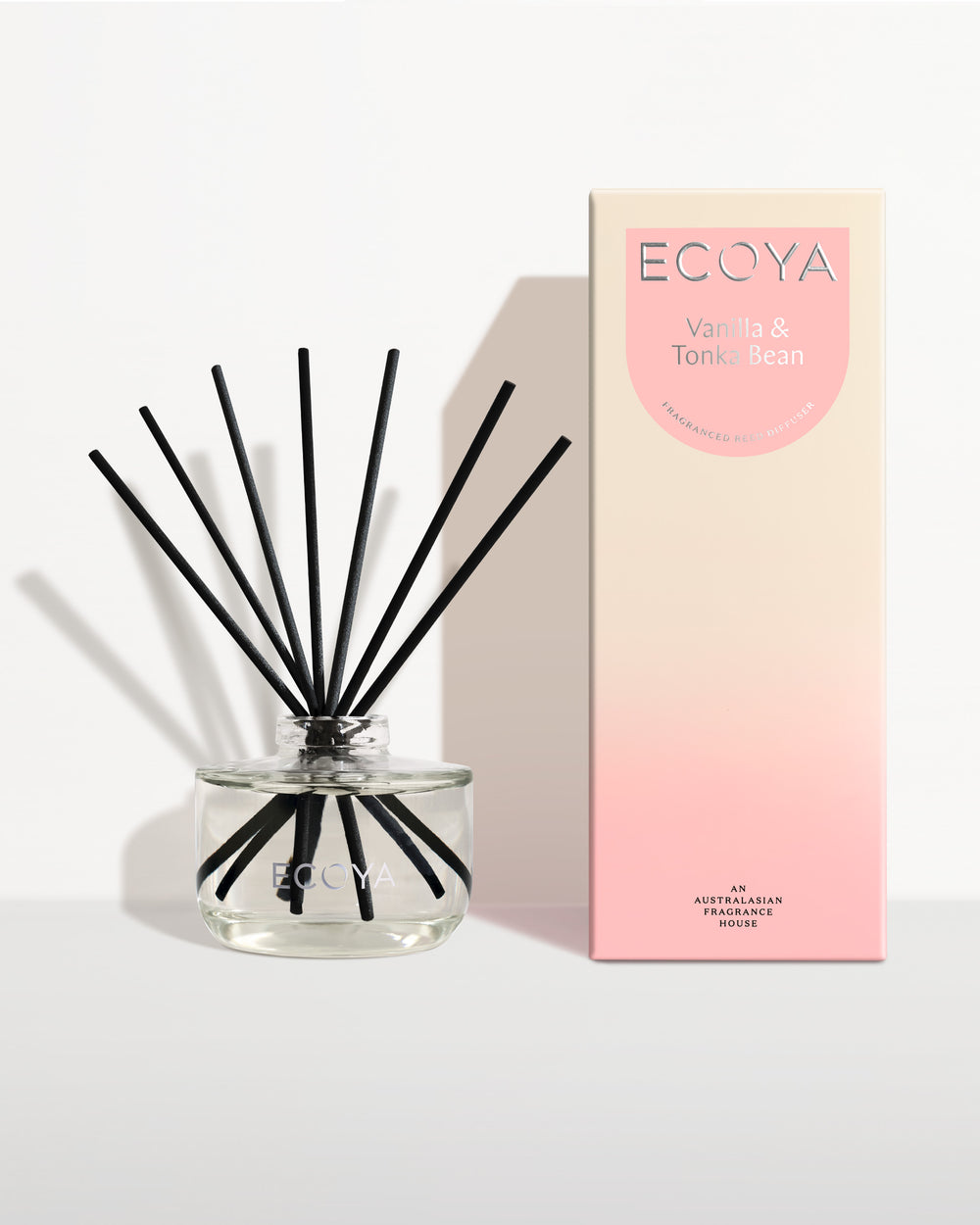 Ecoya Vanilla and Tonka Bean reed diffuser in a clear glass jar with black reeds, beside its blush gift box
