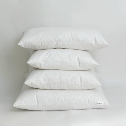 Four feather cushion inners stacked in graduated sizes against a pale wall