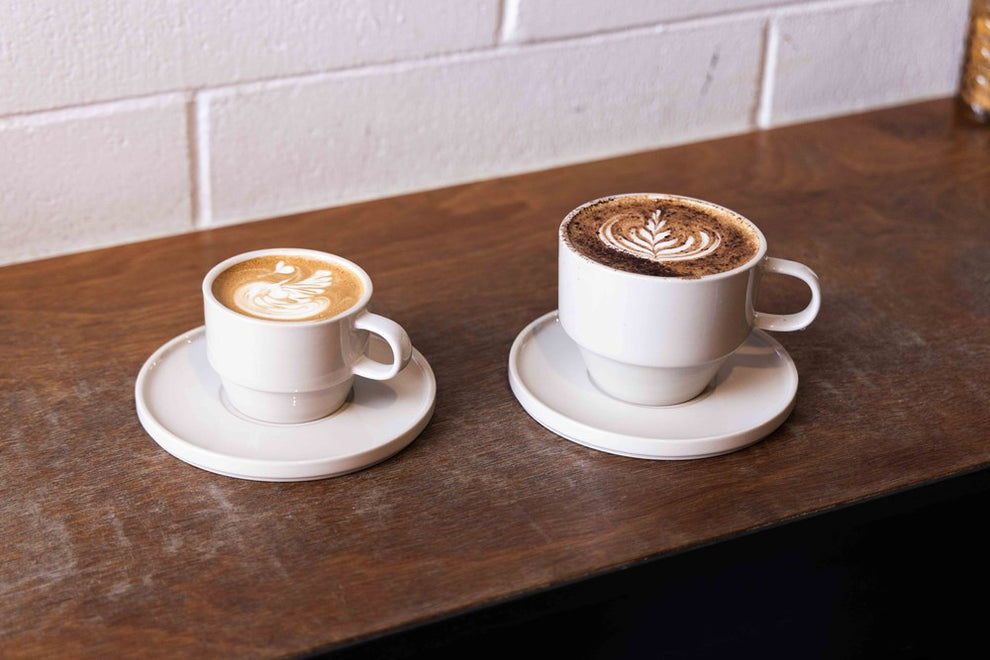 Two Hudson Mugs with latte art on saucers on a wooden bench