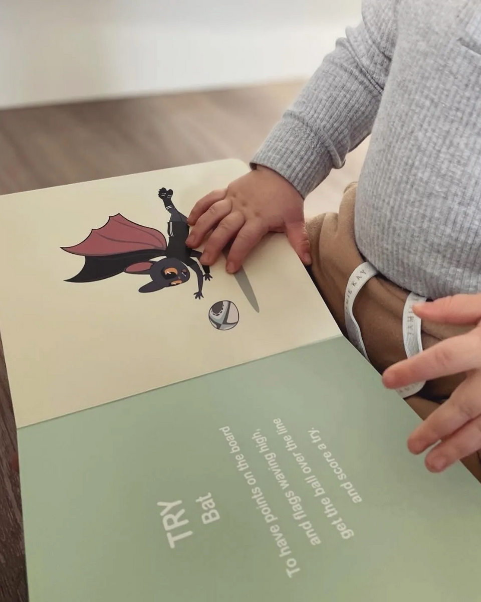 Child's hands on an open Wild About Footy page with an illustrated bird