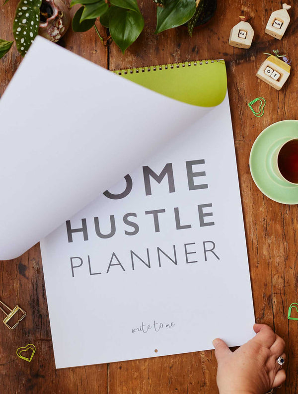 A 2024 HOME HUSTLE PLANNER by Write To Me on a table with a cup of coffee.