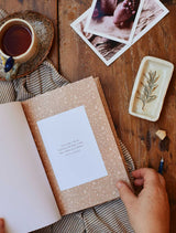 A person gently flipping through Daily Log pages of a newborn life Baby Tracker Journal, displayed on a rustic wooden table.