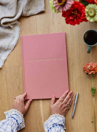 Hands resting on the closed blush linen photo journal on a timber table