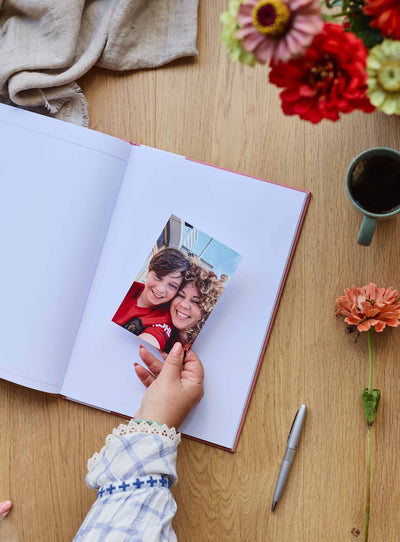 Hand placing a photograph onto a blank page of the journal