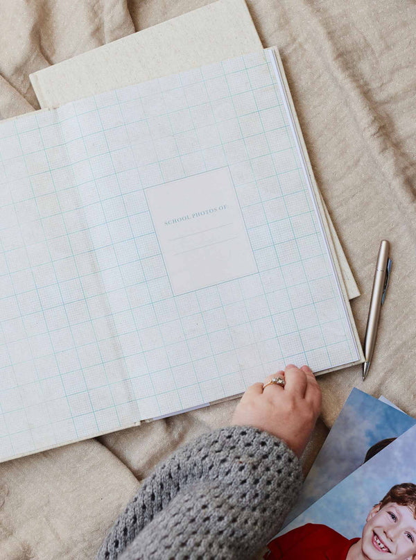 Hands opening the School Photos journal on a knit throw, with a school portrait tucked inside