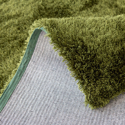 Folded corner of the green shaggy rug showing the grey backing