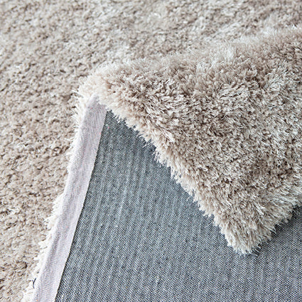 Folded corner of the taupe rug showing the long pile and grey backing