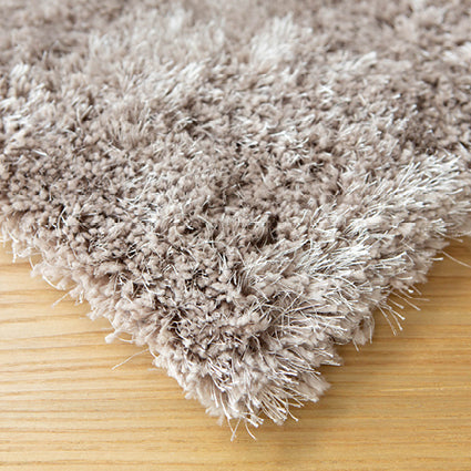 Corner of the taupe shaggy rug on a timber floor showing the pile depth