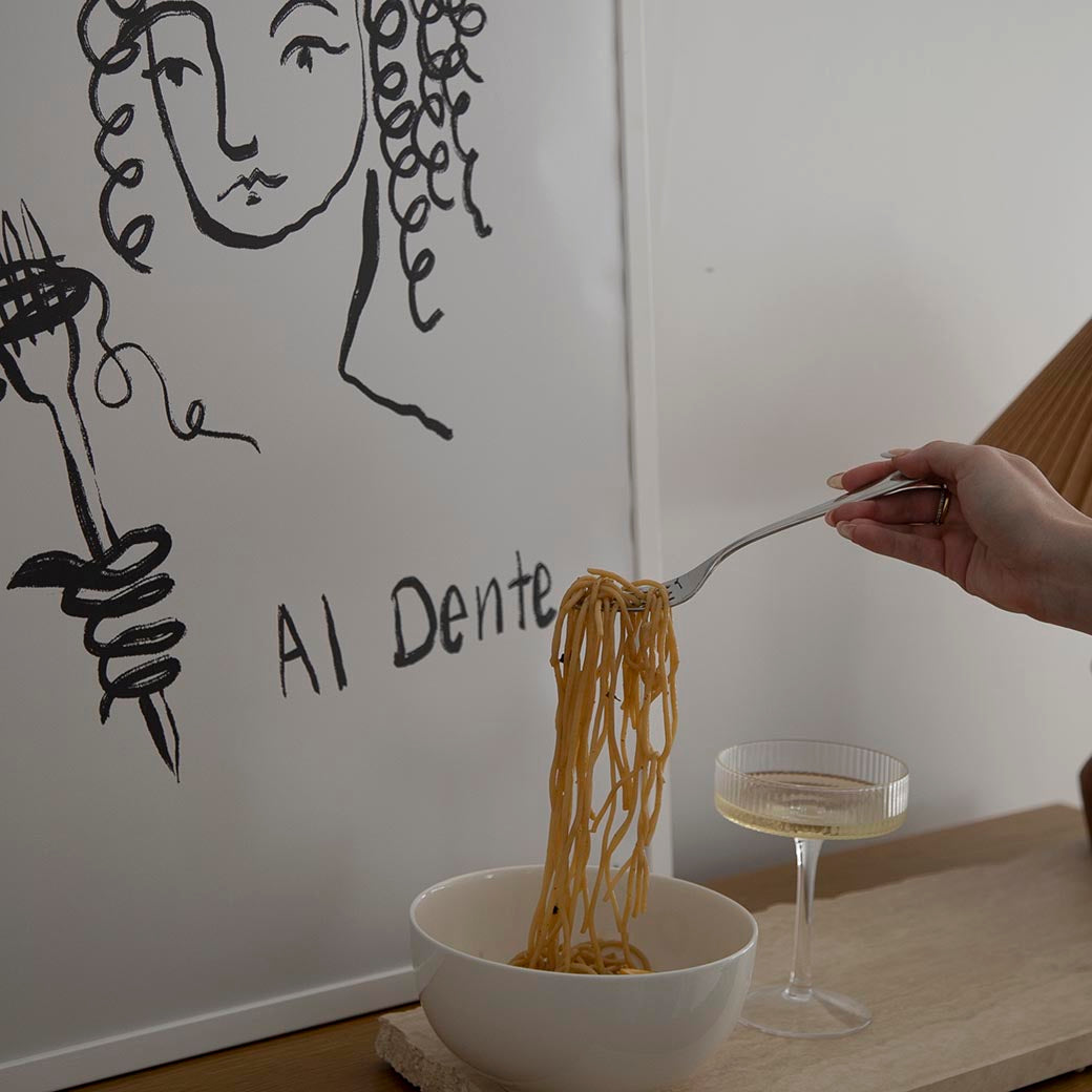 Fork twirling spaghetti from a white bowl in front of the Al Dente print