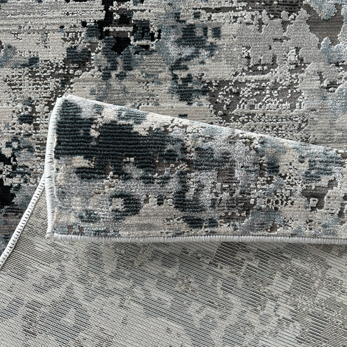 Folded corner of the grey abstract rug showing the low pile and backing