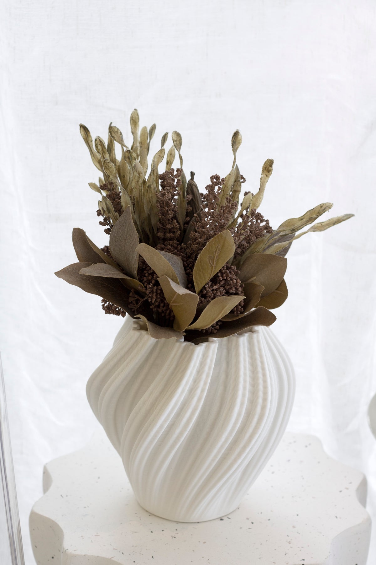 White Amelie fluted vase holding dried brown botanicals on a pale plinth against linen