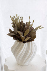 Amelie 3D printed ceramic vase in matte white with rippled wave texture holding dried ruscus and rice flower botanicals on a terrazzo surface against a soft white linen backdrop.