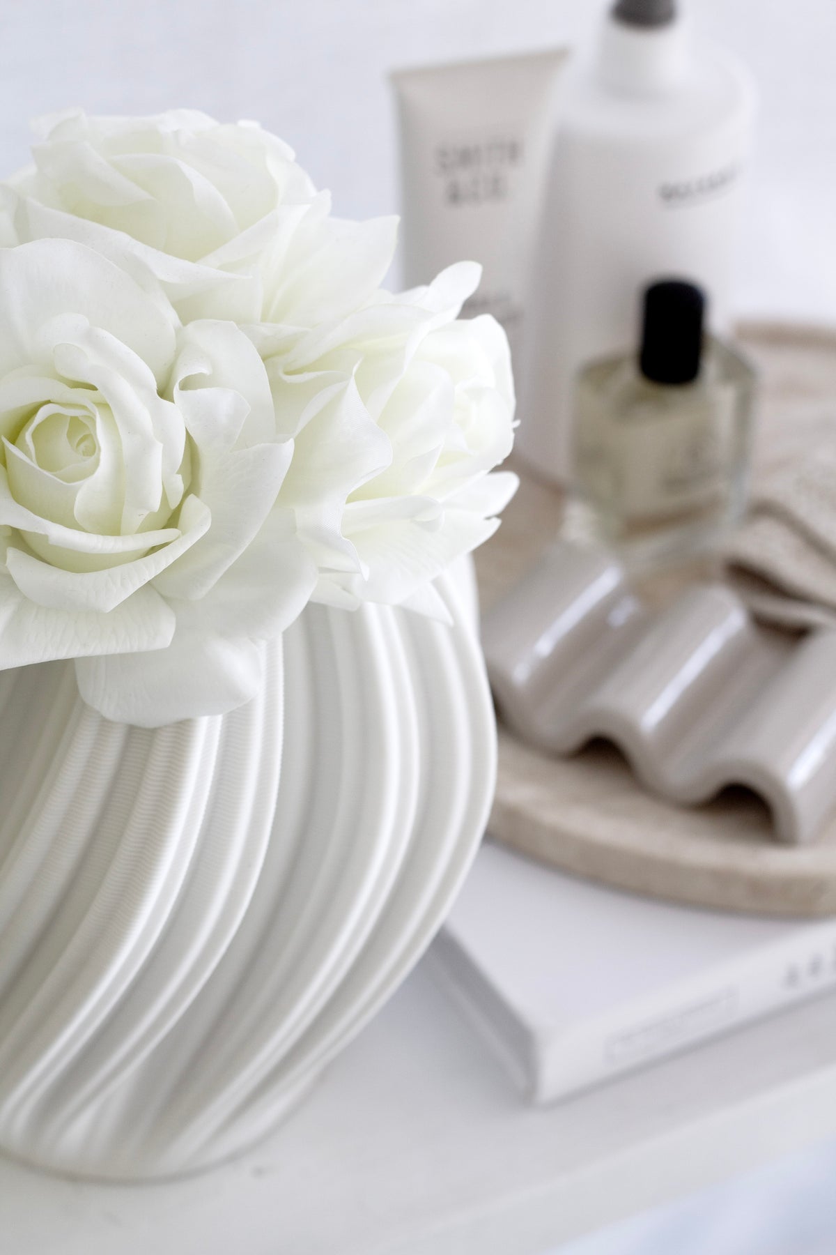 White Amelie fluted vase holding white roses on a vanity beside skincare and nail polish