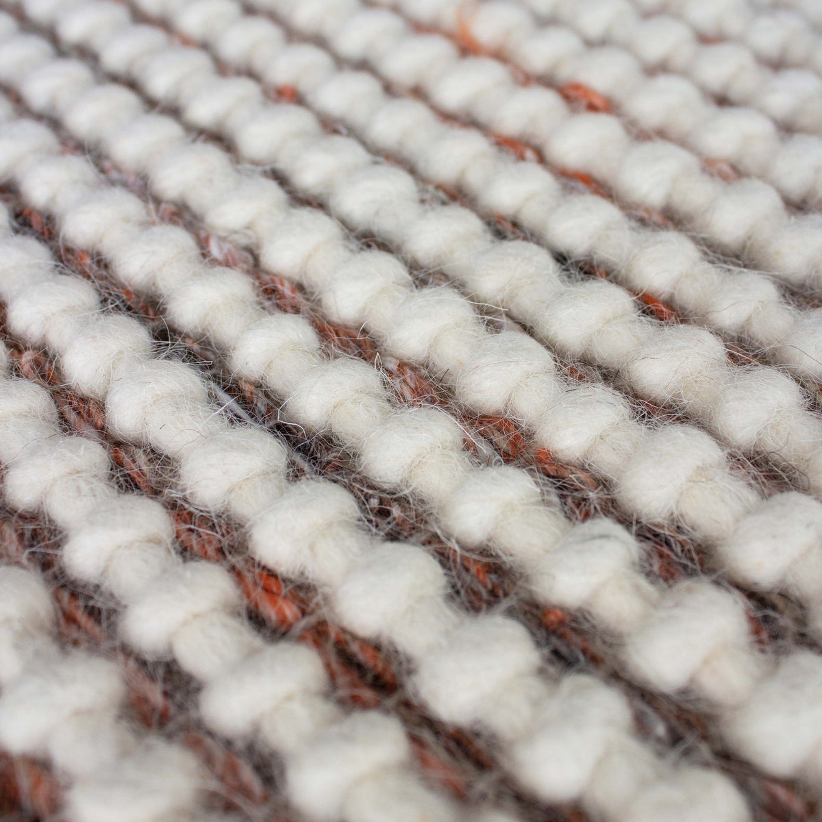 Close view of plump ivory wool loops with thin rust lines between the rows