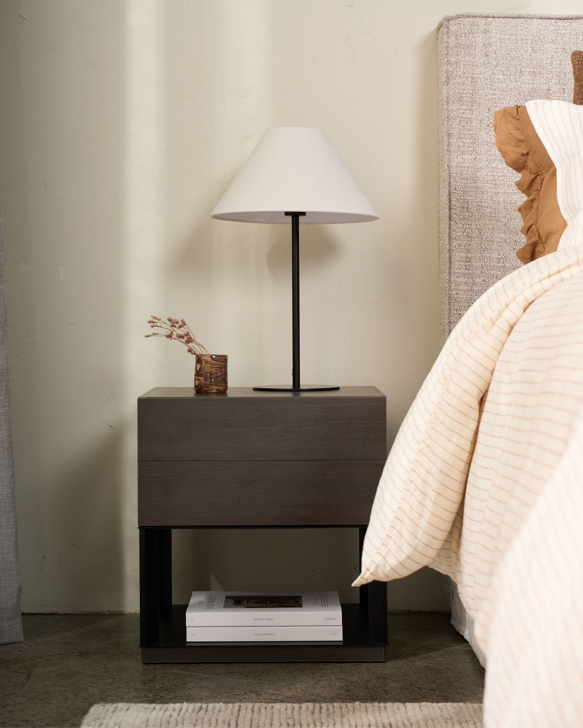 Arch Table Lamp on a dark bedside table beside a neutral bed with layered linen bedding