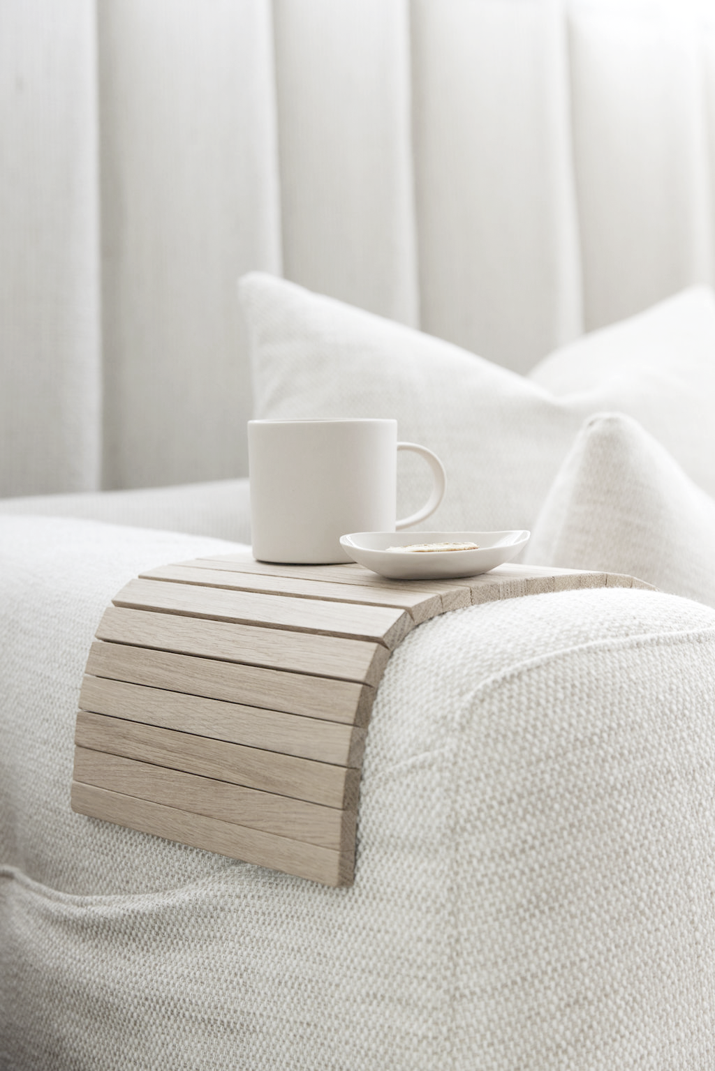 Flexible oak sofa arm tray with a coffee cup on a neutral armchair