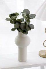 Artificial bluegum eucalyptus bush with rounded sage green leaves arranged in a speckled white sculptural vase on a white surface beside a gold lamp base