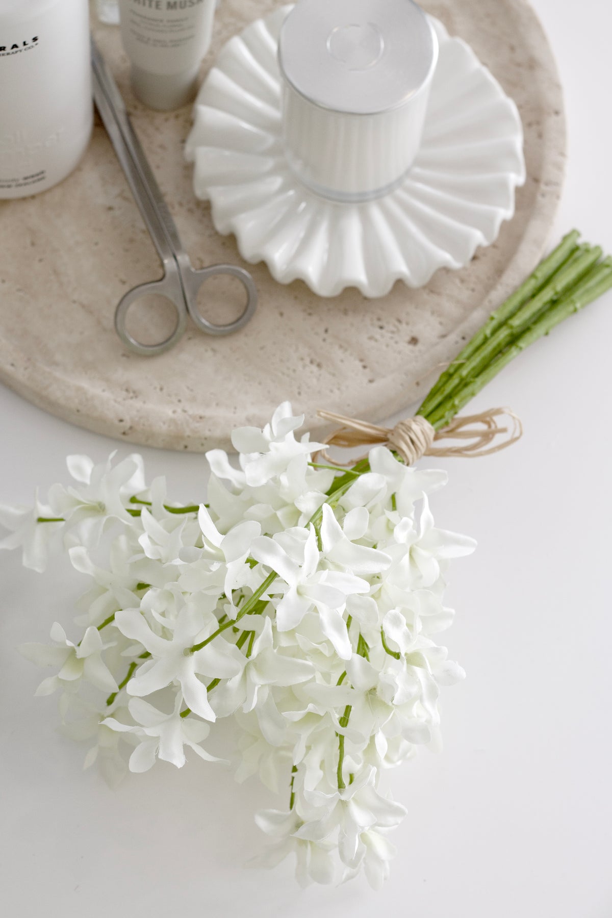 White artificial dendrobium orchid bundle styled on a stone tray with candle, scissors, and neutral beauty products – spa aesthetic