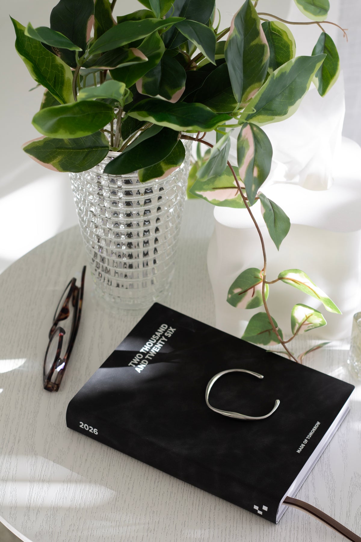 Pothos in a textured white vase on a round table with a black planner and sunglasses