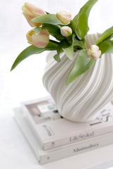Artificial pink and white tulip bouquet in textured white vase styled on stacked neutral books