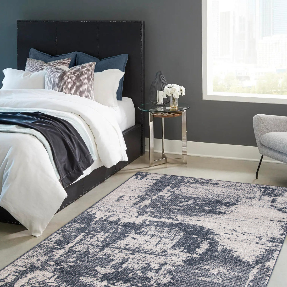 Dark blue and cream rug beside a bed with white linen, a navy throw and a glass side table