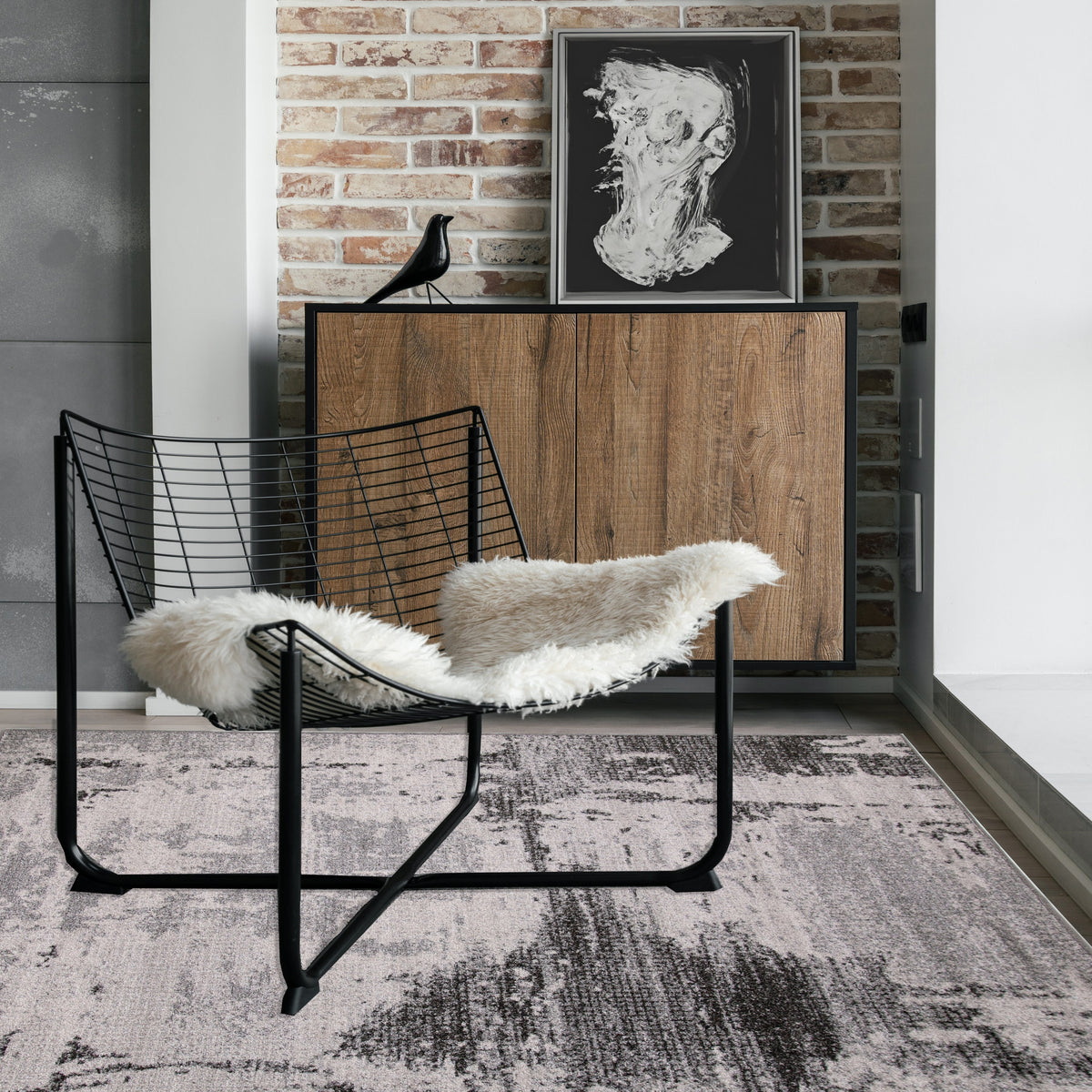 Light grey and black rug under a black wire chair with a sheepskin, beside a timber sideboard and brick wall