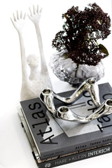 Atlas: Tadao Ando architecture book on a stack with silver candle holder, white sculpture and dark foliage in a glass vase.