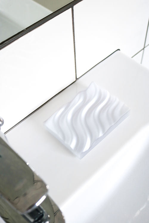 A white Ripple Soap Tray with a wave pattern made from recycled PLA plastic, designed by Utilize Studios.