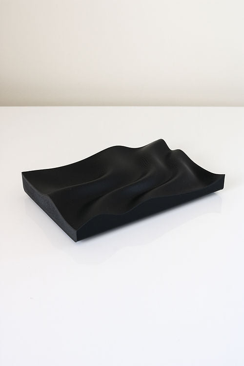 A black Utilize Studios Tidal Tray with a wavy design, made from recycled plastic.