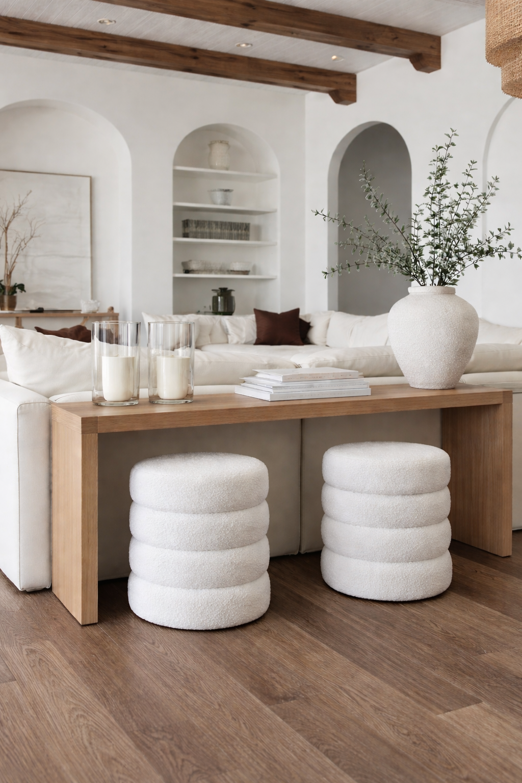 Two white tiered ottomans tucked under a timber console in a bright open room