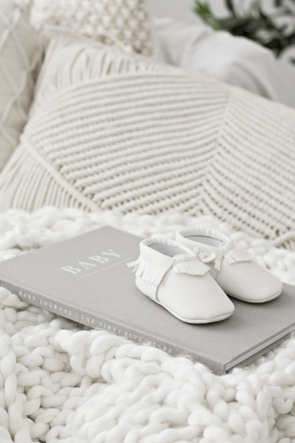 Grey linen Write To Me Baby journal on a chunky white knit blanket with tiny white baby moccasins