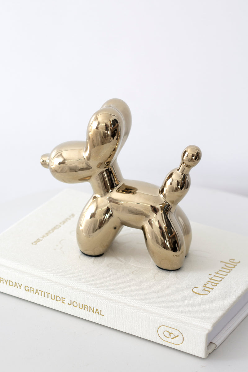 Gold ceramic balloon dog sculpture styled on top of a white gratitude journal for playful modern home décor