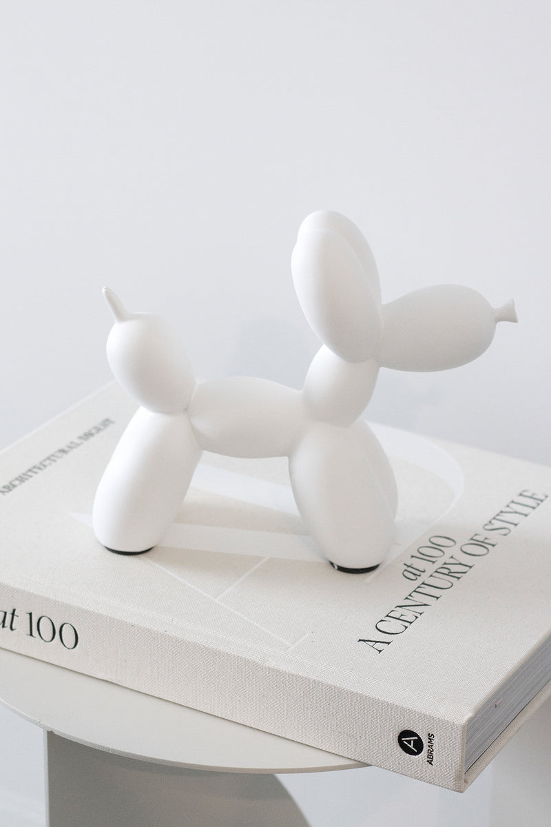 White ceramic balloon dog sculpture styled on coffee table book; playful modern decorative ornament for home styling.