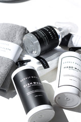 Flatlay of Barkly Basics black and white hand wash, dish wash and cleaning products with grey cloths and bright shadows on a white surface.