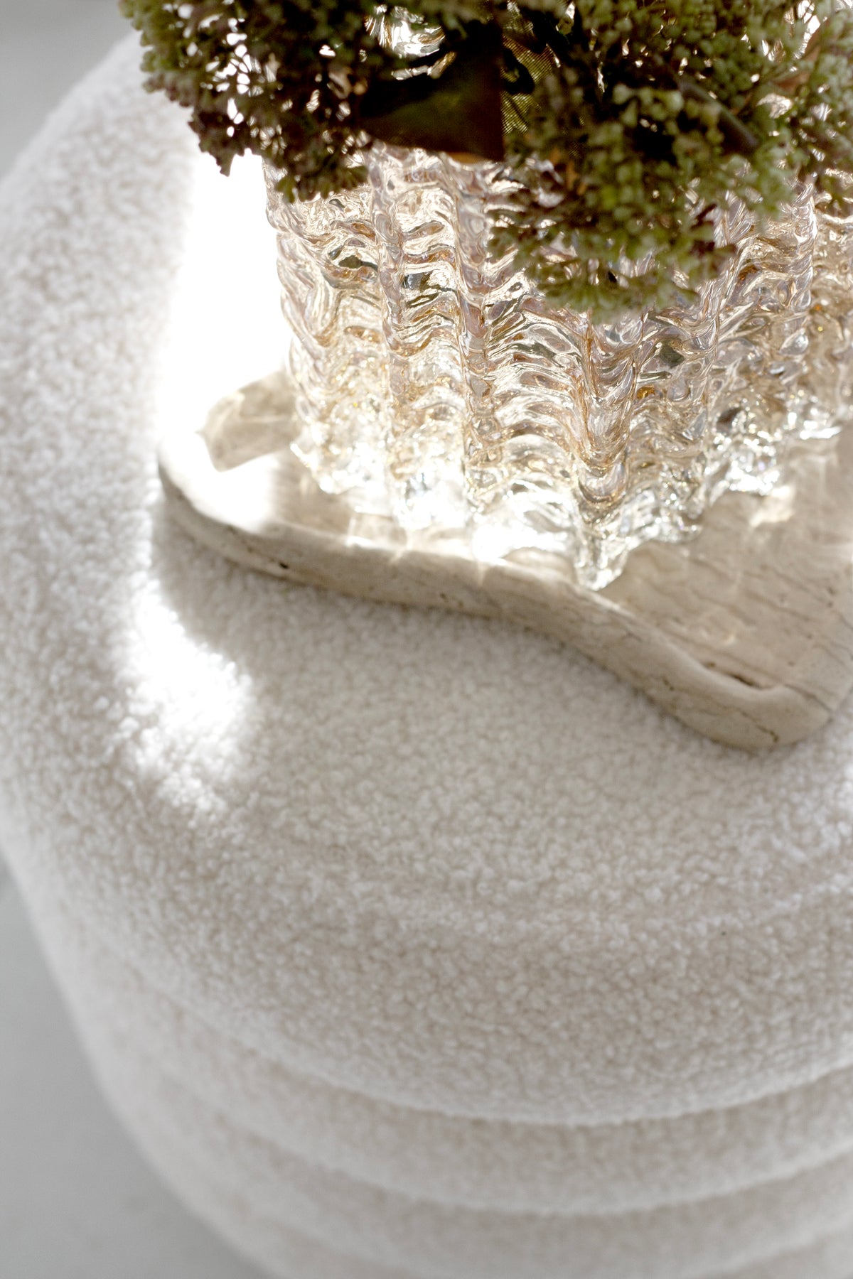 Close on the white boucle texture, a glass vase and a driftwood piece resting above