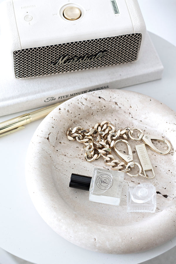Bay round tray with natural stone look, styled with gold chain, perfume oil, and neutral décor on a white surface.