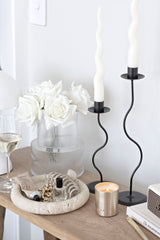 Round travertine tray styled on a wooden console with white roses, beauty items, a candle and sculptural black candlesticks
