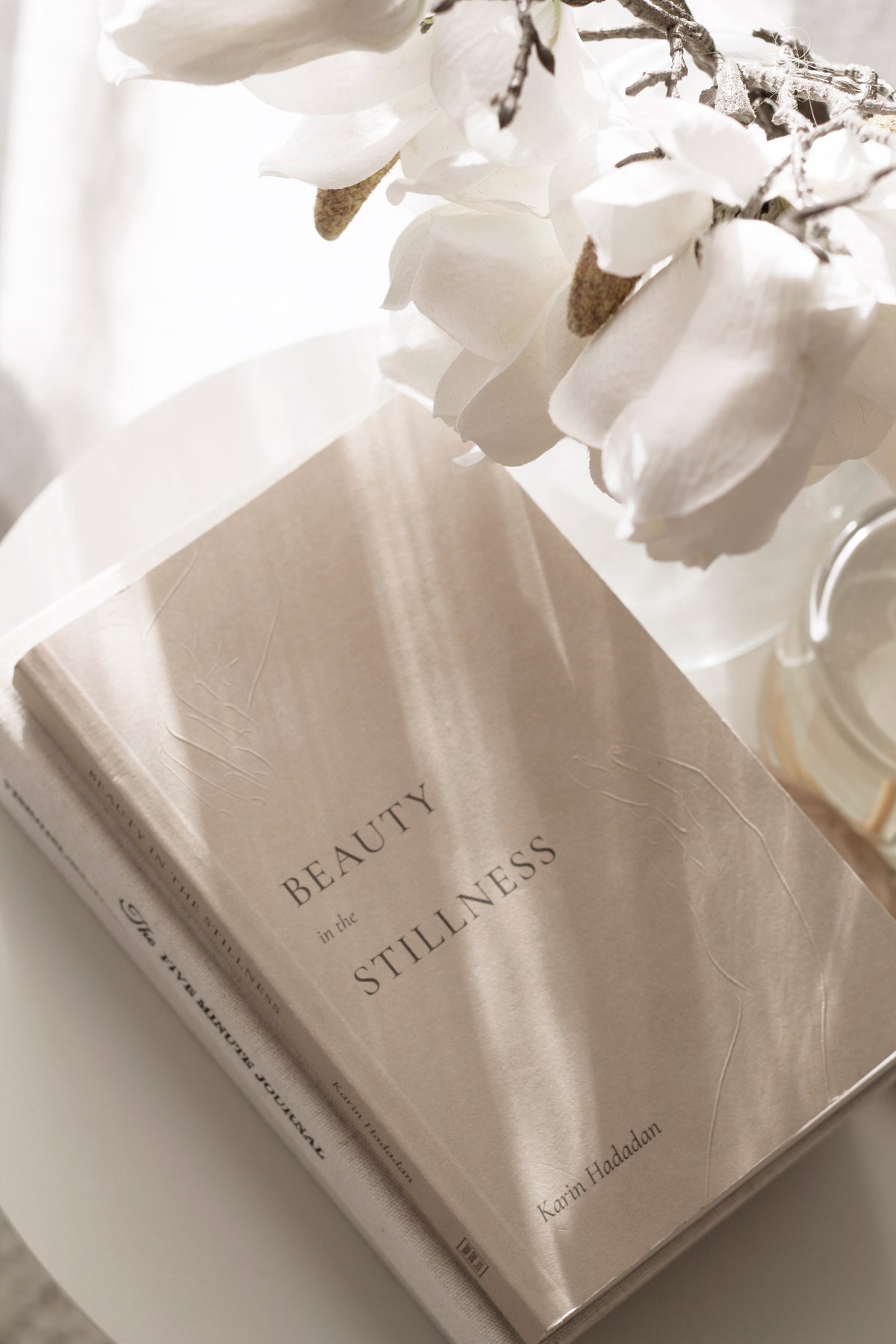 Beauty in the Stillness book by Karin Hadadan – poetry for mindfulness, healing, and calm living with white flowers in the background