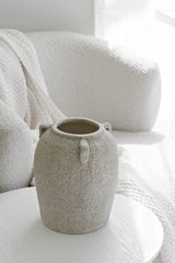 Sculptural beige vase styled beside a white boucle armchair in a soft neutral interior
