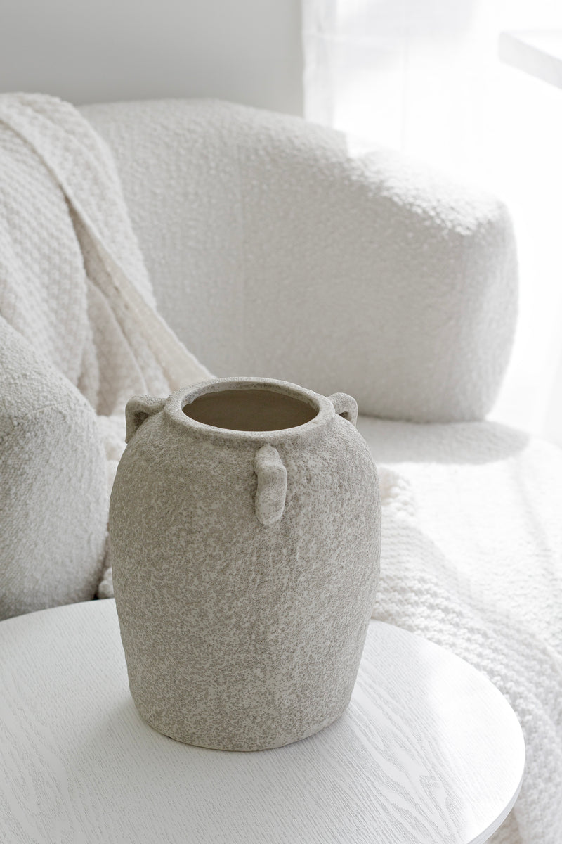 Sculptural beige vase styled beside a white boucle armchair in a soft neutral interior